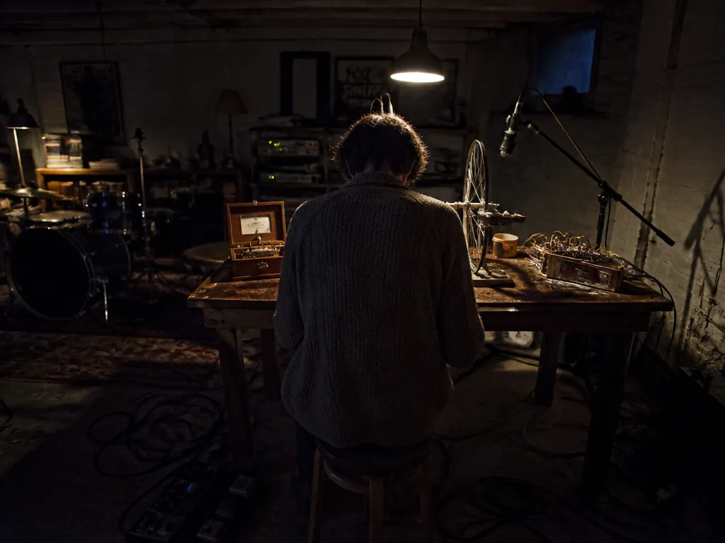 Photorealistic wide-angle interior shot of a cramped basement music room at night, seen from…