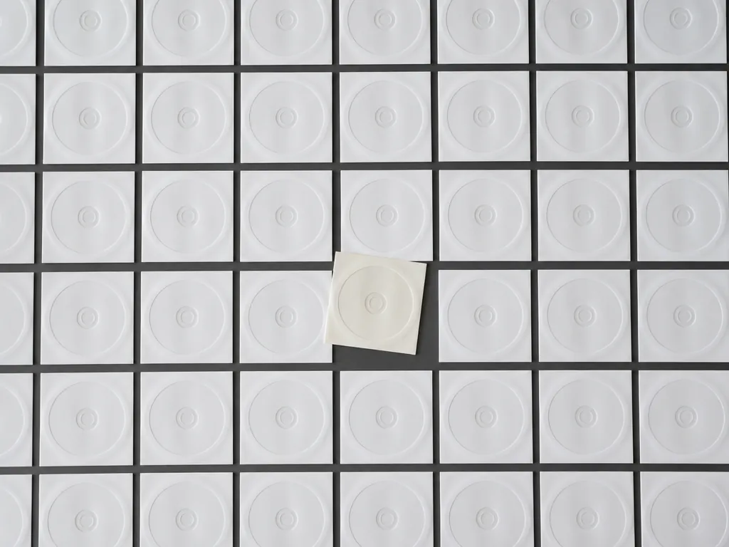 An overhead flat-lay photograph of a long grid of identical unlabeled white CD sleeves…