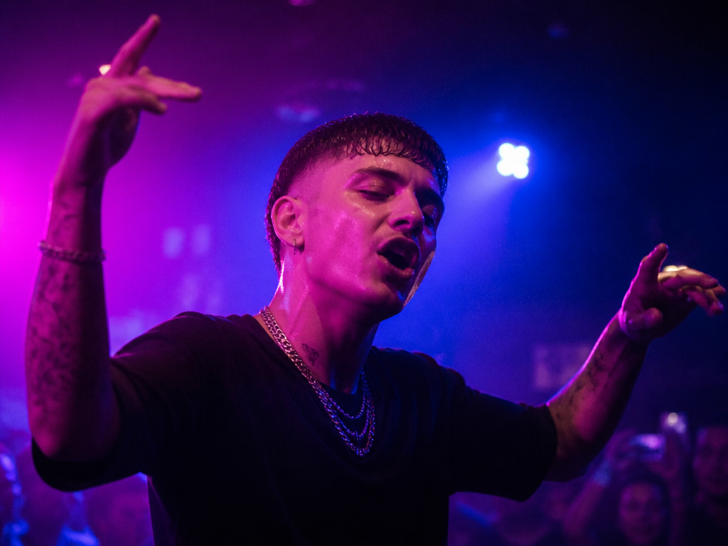 A young Italian rapper performing in a dim underground Milan club at night, captured…